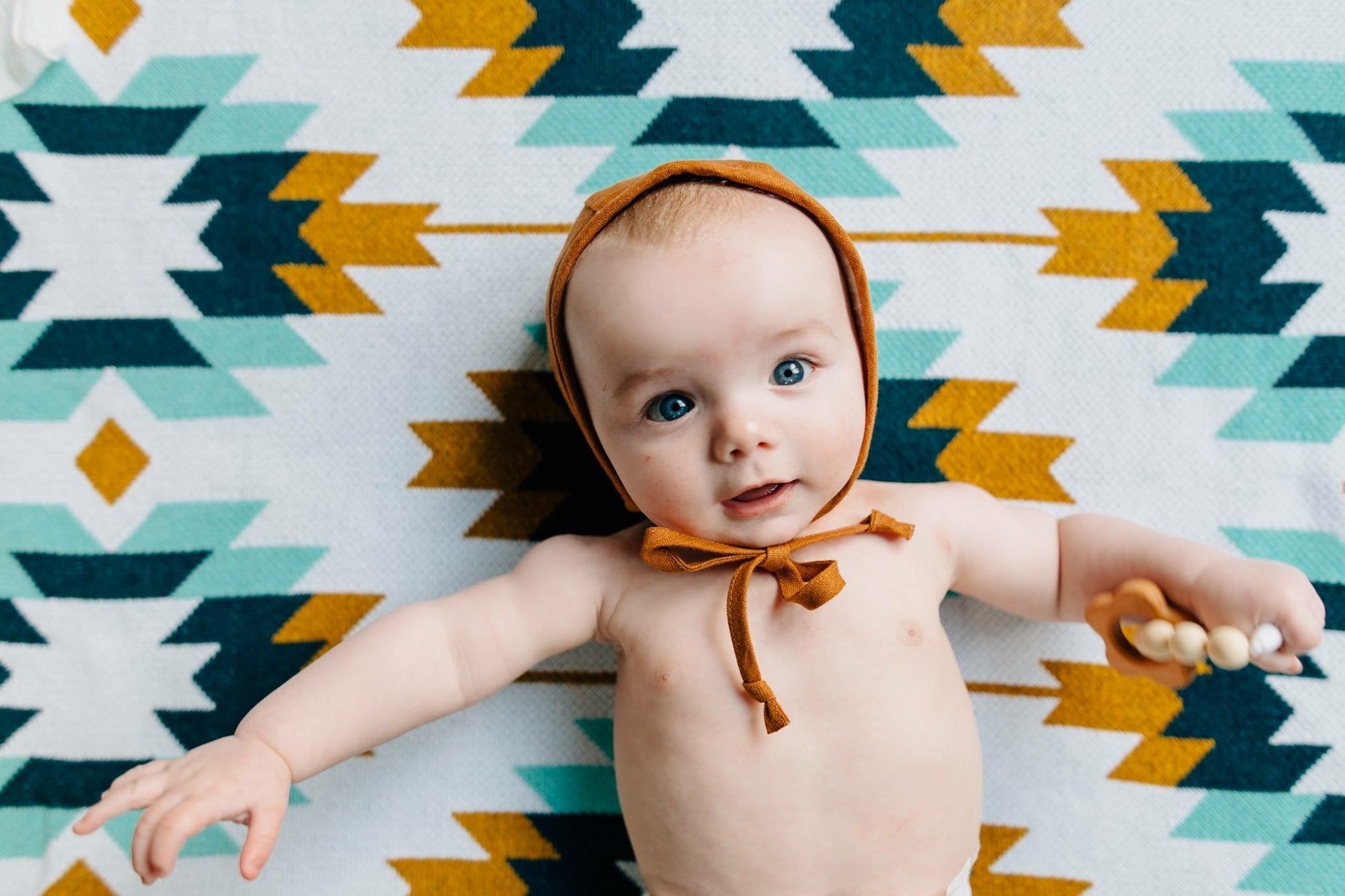 A cute baby laying on top of a Seek & Swoon Sedona Baby Blanket
