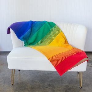 Seek & Swoon Rainbow Pride Throw blanket on a white leather couch