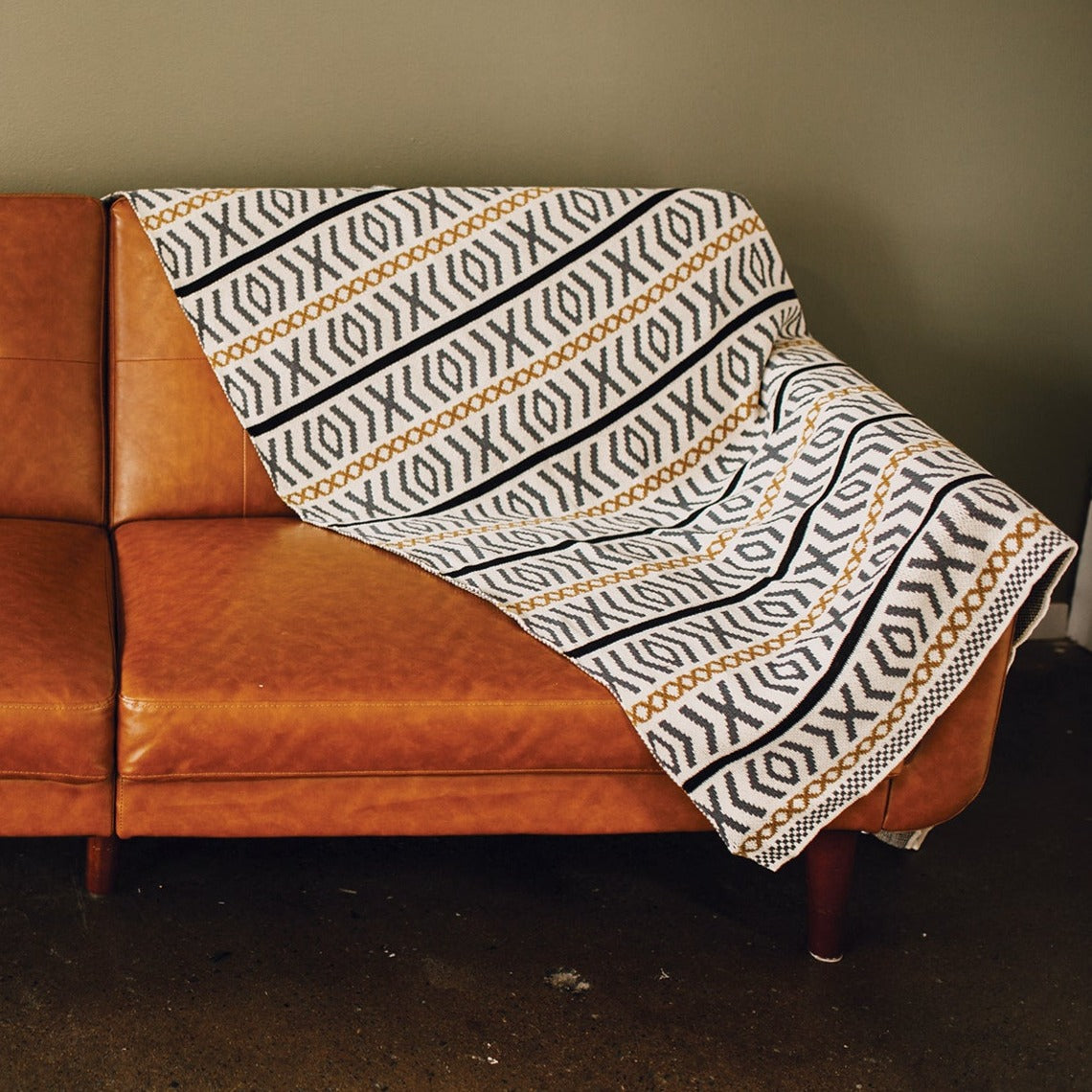 Seek & Swoon Otok Throw draped over a brown leather sofa.
