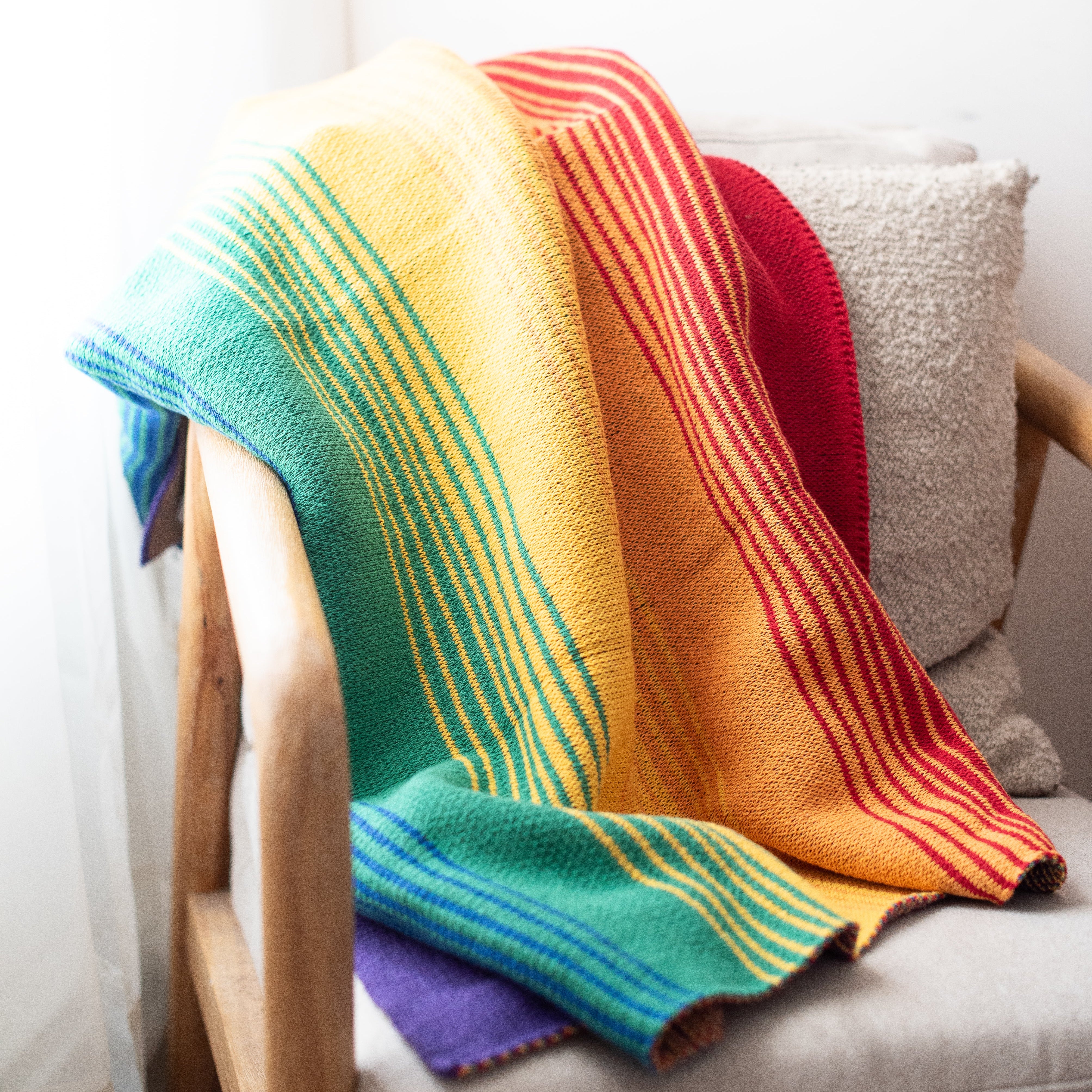 Colorful rainbow striped ombrés blanket draped over a chair with a neutral background